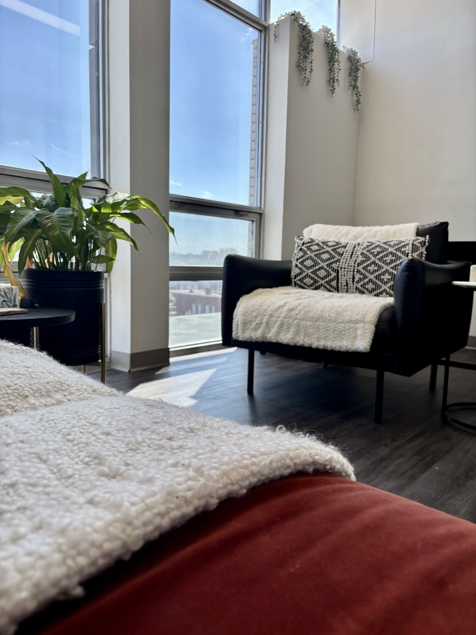 Un fauteuil noir garni d’une couverture blanche, une plante verte et de grandes fenêtres donnant sur la ville, dans un bureau de la clinique.